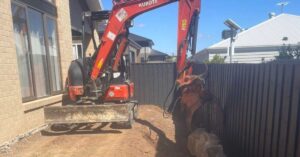 Excavator lining up large rocks beside a fence