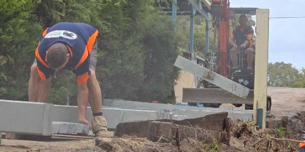 Two construction workers installing concrete retaining wall panels
