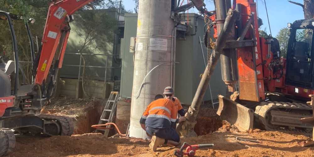 Workers using excavators in installing large poles